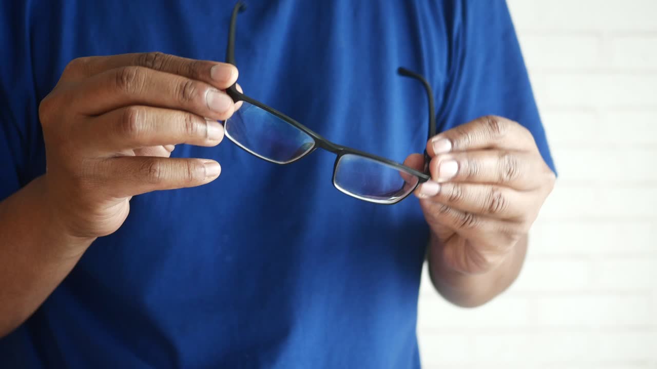una persona sosteniendo gafas frente a una pared blanca