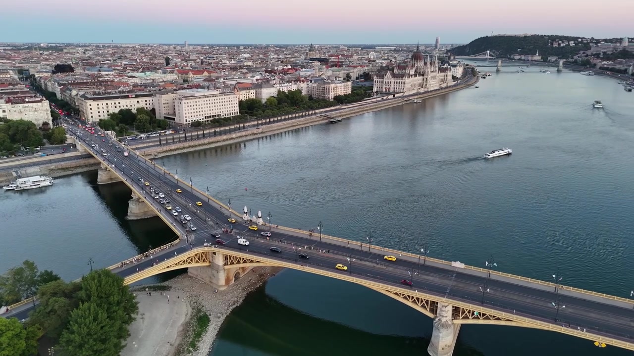 Paesaggio urbano di Budapest al crepuscolo con il Ponte Margherita, il Palazzo del Parlamento ungherese e il Danubio accanto all'Isola Margherita, luci della città e traffico visibili in una vista aerea