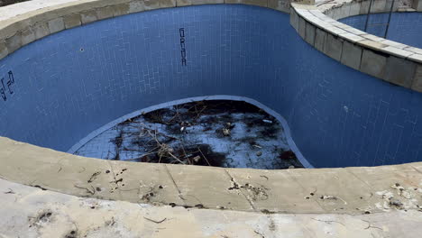 Suciedad-En-El-Fondo-De-La-Piscina-Vacía-Abandonada-Y-En-Ruinas,-Vista-De-ángulo-Alto