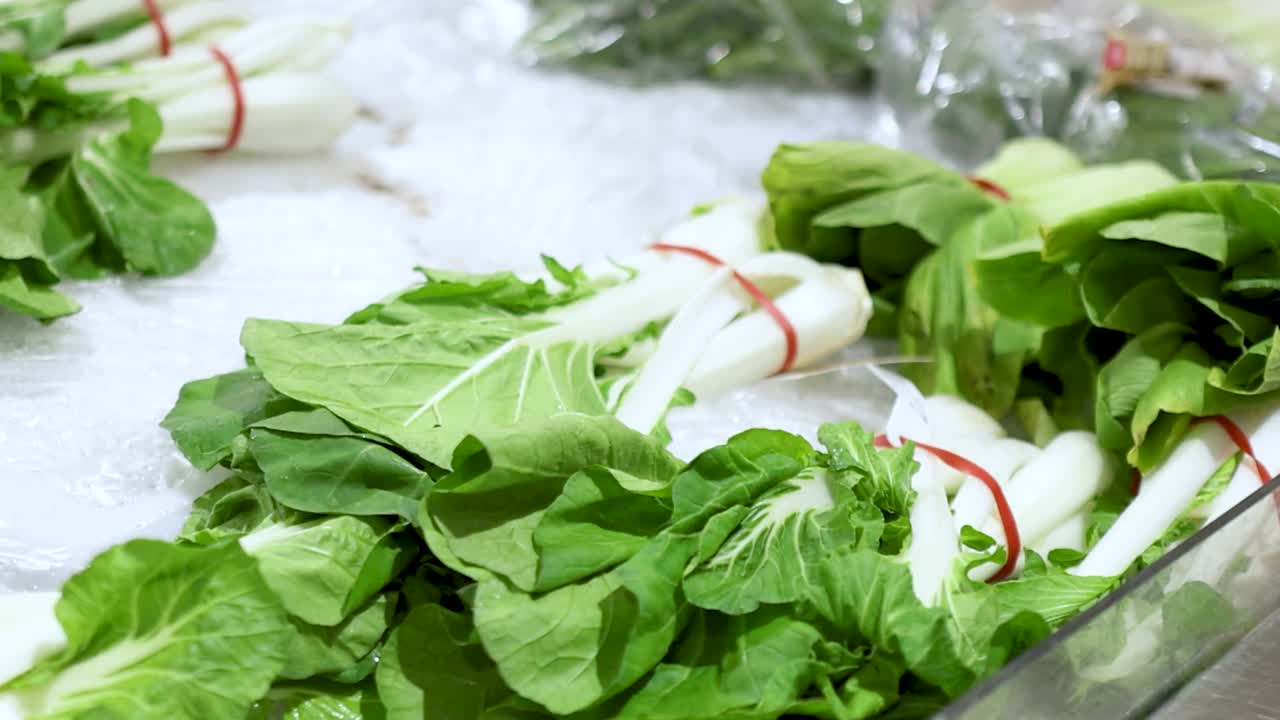 Die Hand eines Käufers nimmt frischen grünen Pak Choi aus einer Eisvitrine im Supermarkt