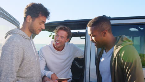 three young men using tablet computer talking by their car