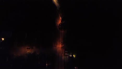 cars on illuminated interstate road of american town at night. orange lighting lantern and streetlamps in quiet suburbia. aerial top down tracking shot.