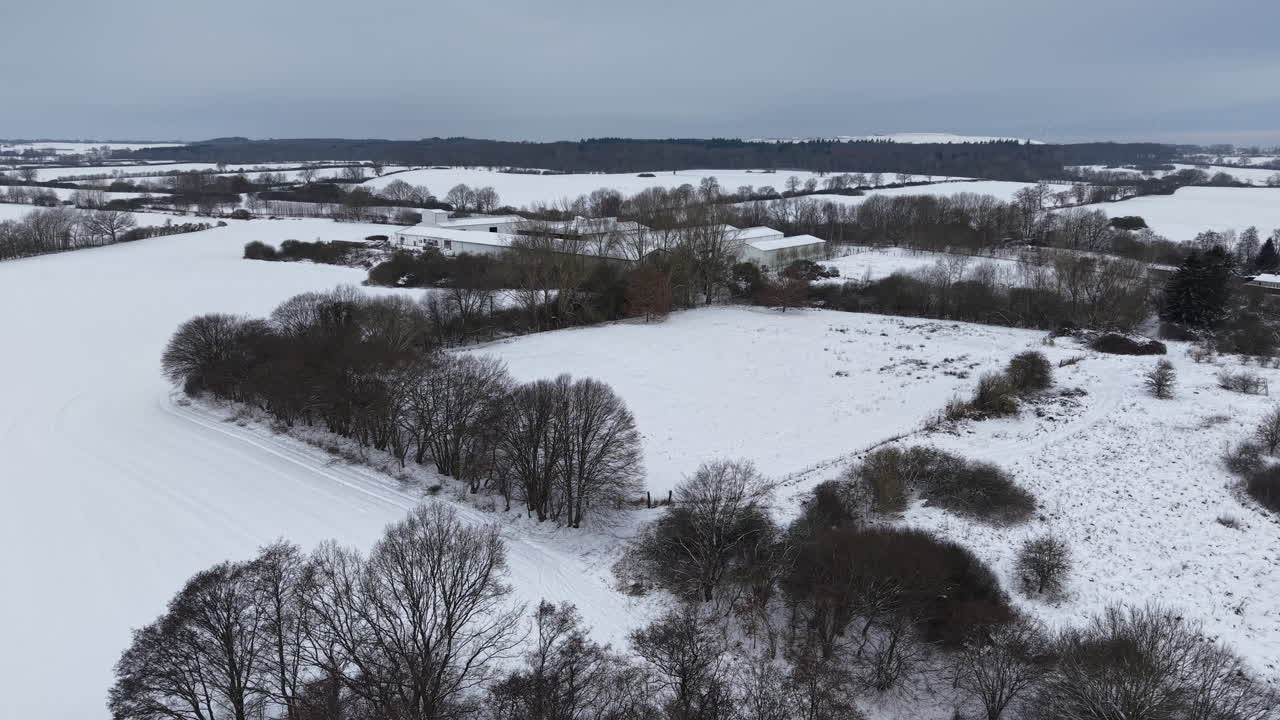 Filmato aereo realizzato con drone che sorvola un lago ghiacciato e una campagna innevata durante l'inverno. Il video mostra un vasto paesaggio invernale con acqua ghiacciata, campi bianchi, alberi e terreno rurale.