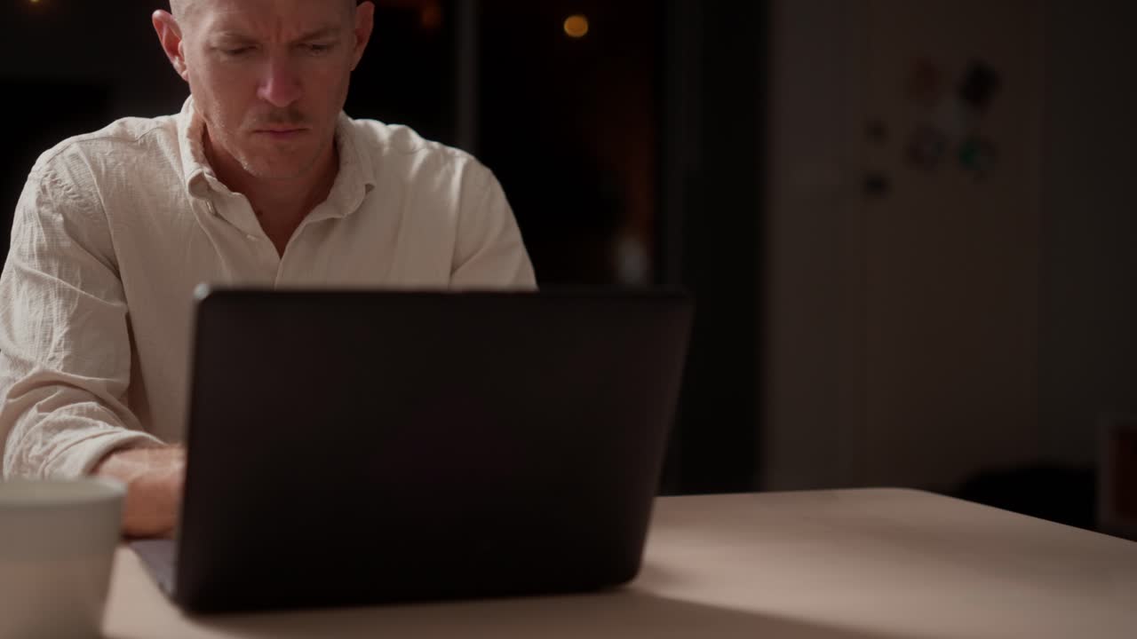 Mand arbejder sent hjemme, uvidende om en mistænkelig skikkelse udenfor om natten.