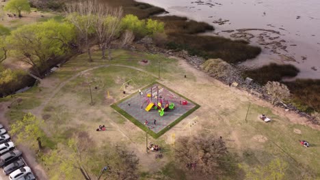 Aerial-orbit-shot-of-children-playing-in-park-near-river-shore-in-Buenos-Aires-at-sunlight