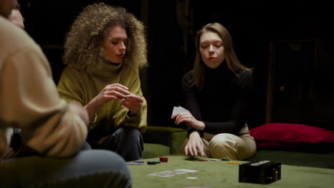 Camera-Focuses-On-Two-Women-Playing-Poker-With-Friends-Sitting-On-The-Couch-In-The-Living-Room