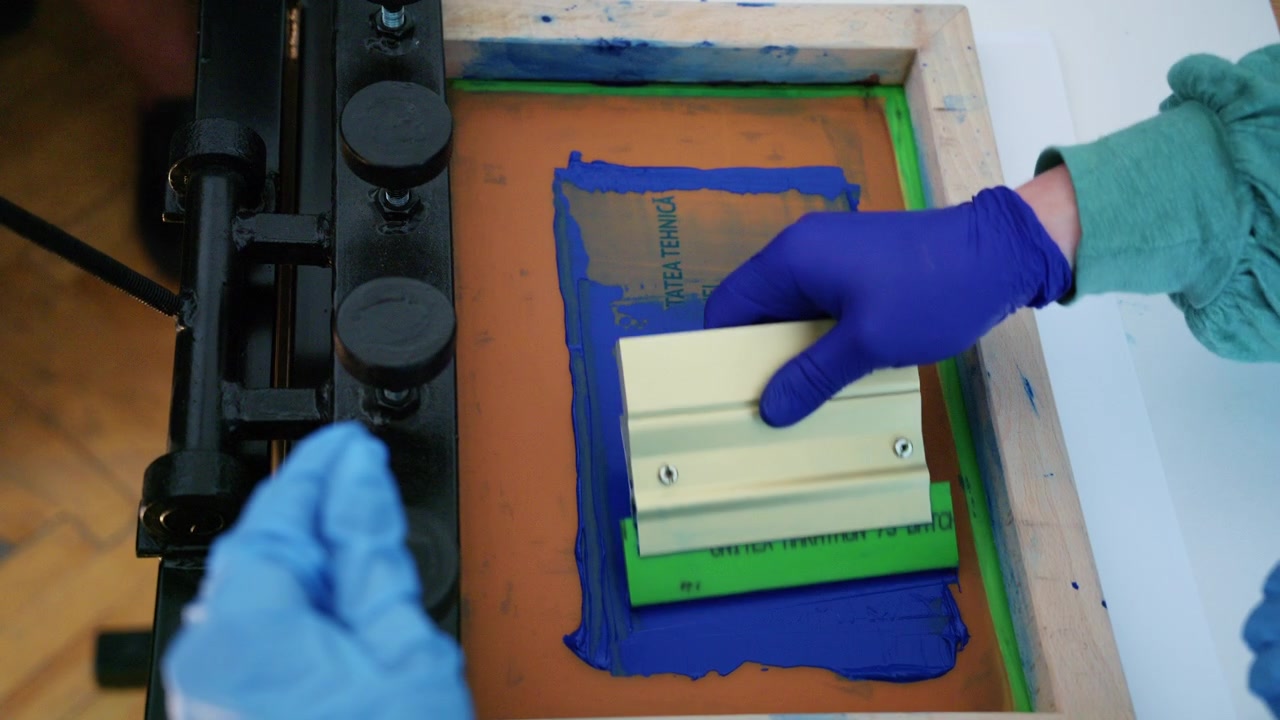 Tekstil üretimi sırasında bir serigrafi çerçevesi üzerine mürekkep yaymak için rakle kullanan işçi.