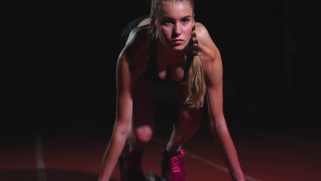 Female-athlete-on-a-dark-background-is-preparing-to-run-the-cross-country-sprint-from-the-pads-on-the-treadmill-on-a-dark-background