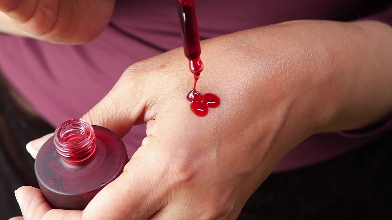 Primer plano de un sérum facial rojo cayendo sobre una mano.
