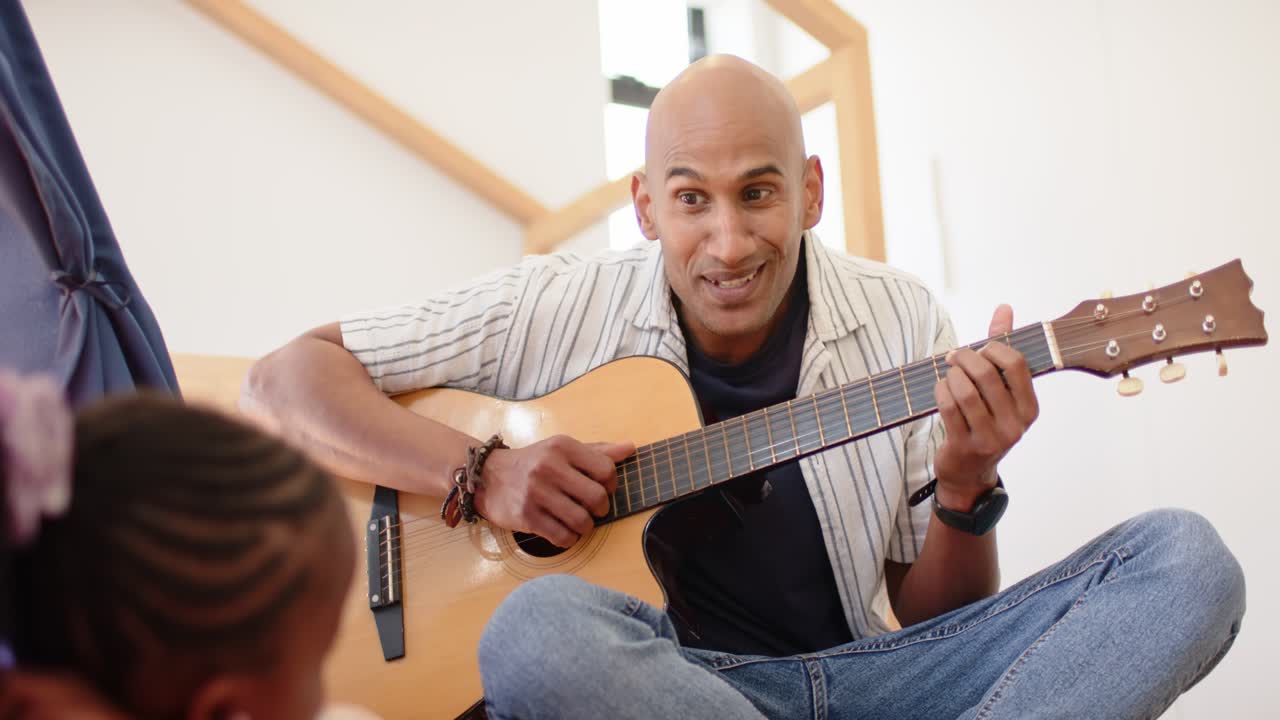Padre che guarda la figlia mentre tocca gli accordi della chitarra, suonando e insegnando musica in salotto
