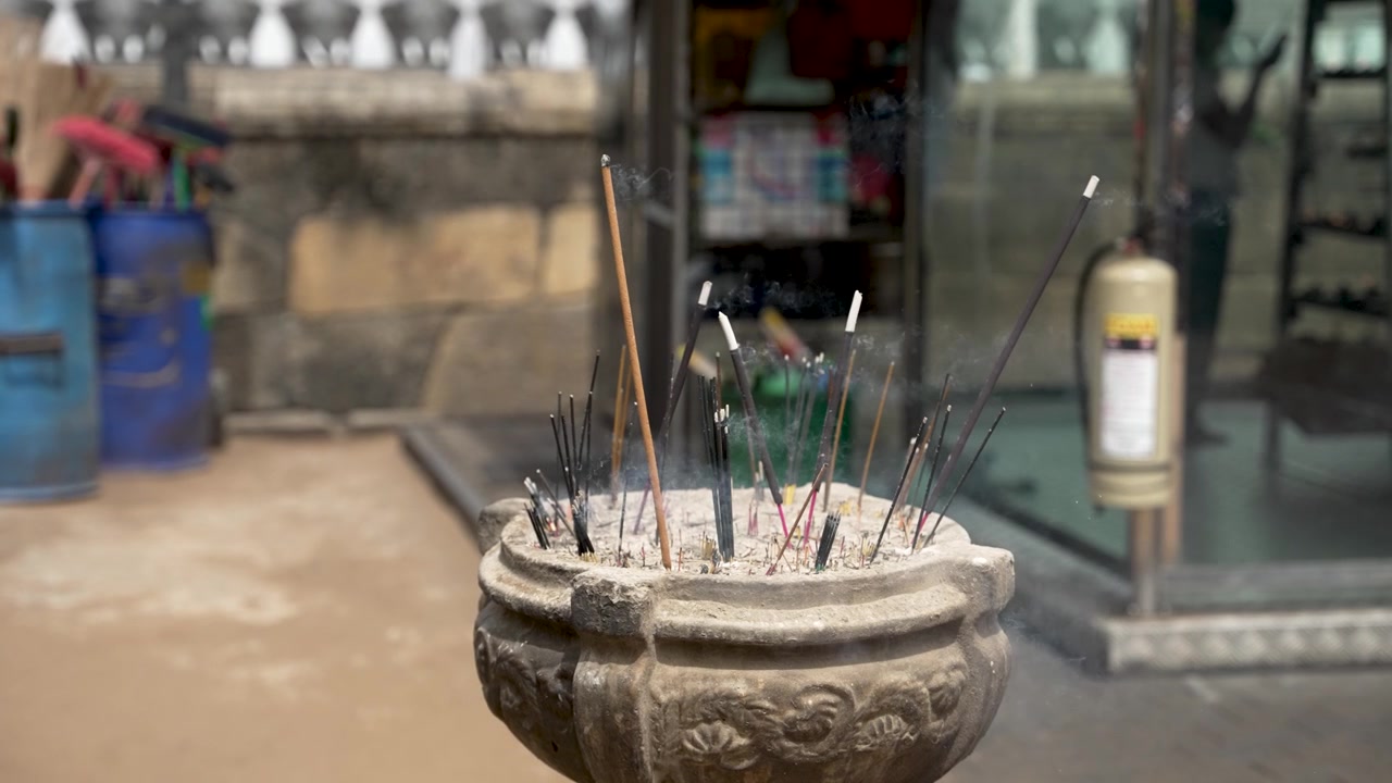 Primo piano di bastoncini d'incenso che bruciano in un'urna in un tempio, circondati da aria fumosa e un'atmosfera sacra. Catturato in un ambiente esterno, che evoca tranquillità e spiritualità.