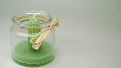 a green cactus candle formed inside the transparent jar with yellow ribbon - close up shot