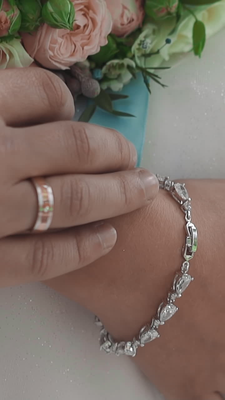 Groom strokes arm and wrist of beloved woman with silver bracelet in white wedding dress closeup slow motion. Young man and lady loving relationship