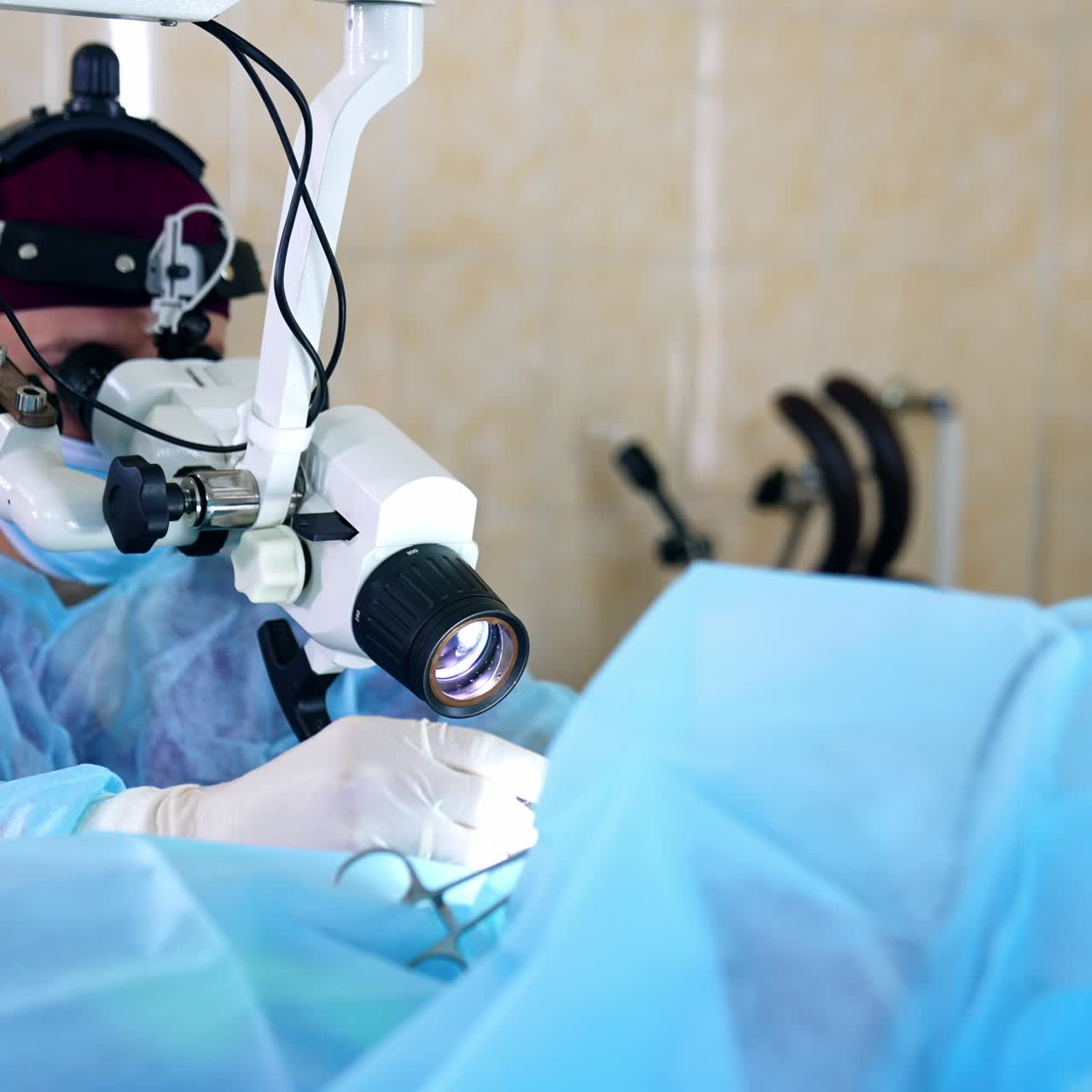 Un medico in divisa blu e mascherina è seduto mentre osserva un microscopio durante una procedura medica. Sfondo sfocato