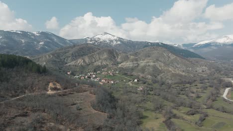 A-drone-shot-of-forest-mountains-with-snow,-warm-weather,-flying-above-a-dreamy-village-hill,-4K-video,-European-winter-nature,-scenic-white-clouds,-beautiful-landscape