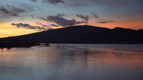 silhouetted bay on uros floating islands in lake titicaca, at sunset with boat, time lapse long shot