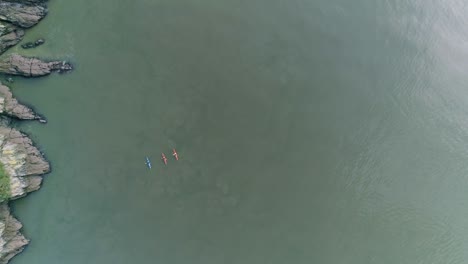 vista aérea de arriba hacia abajo de tres personas en kayaks, uno azul y dos rojos.
