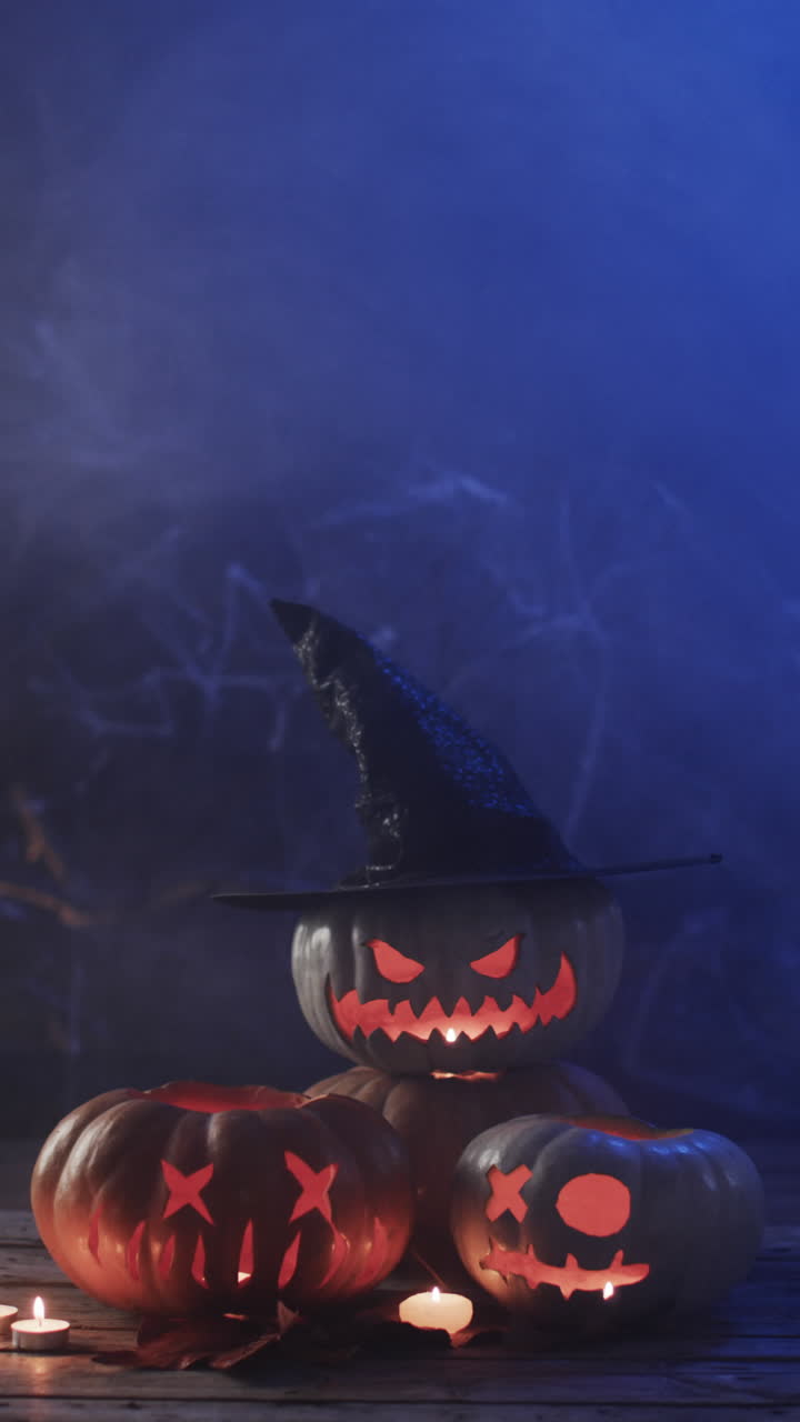 Vertical video of halloween carved pumpkins and smoke with copy space on blue background