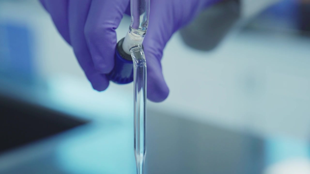 A scientist is pouring a chemical drop by drop in a beaker using a pipette.