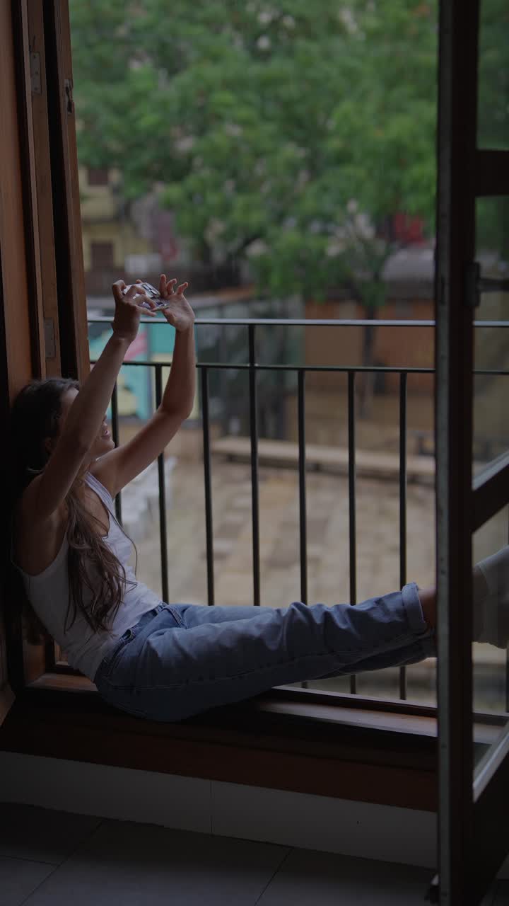 mujer tomando una foto en un día de lluvia desde el balcón