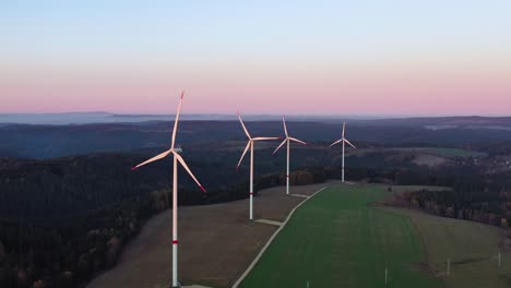 aerial view of wind turbines and spinning rotor blades in landscape at twilight