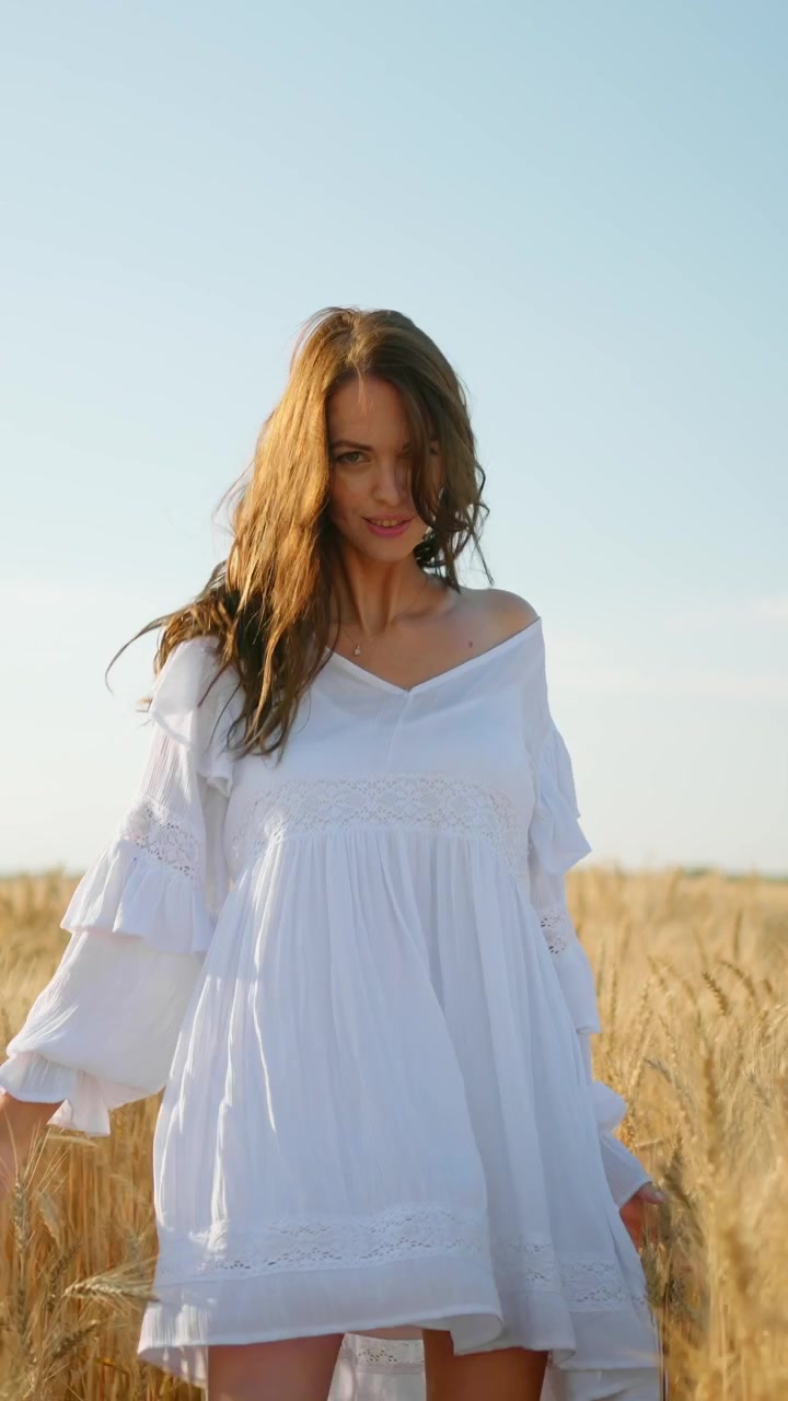 Giovane donna in abito bianco che cammina attraverso un campo di grano dorato