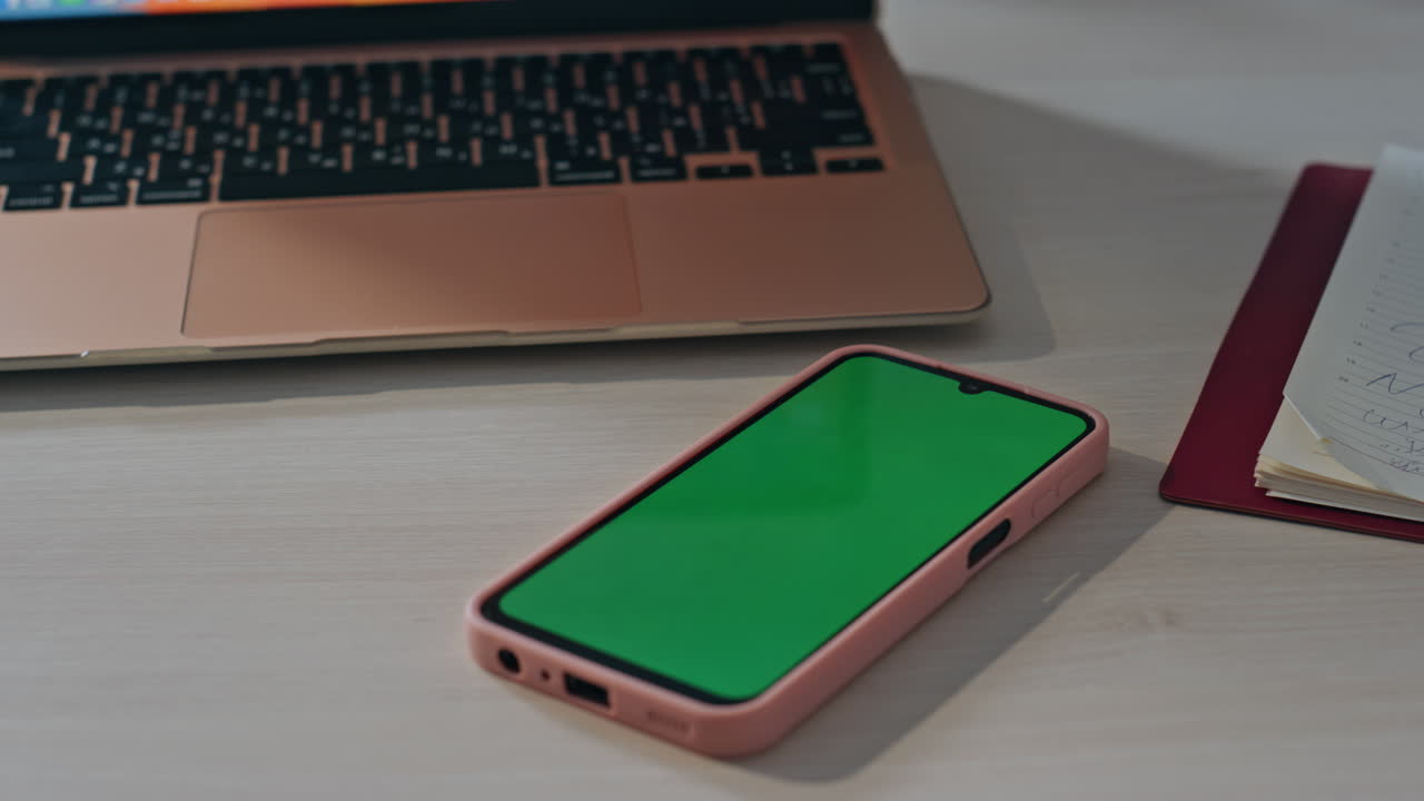 Chroma key cellphone placed on office desk near turned laptop computer close up.