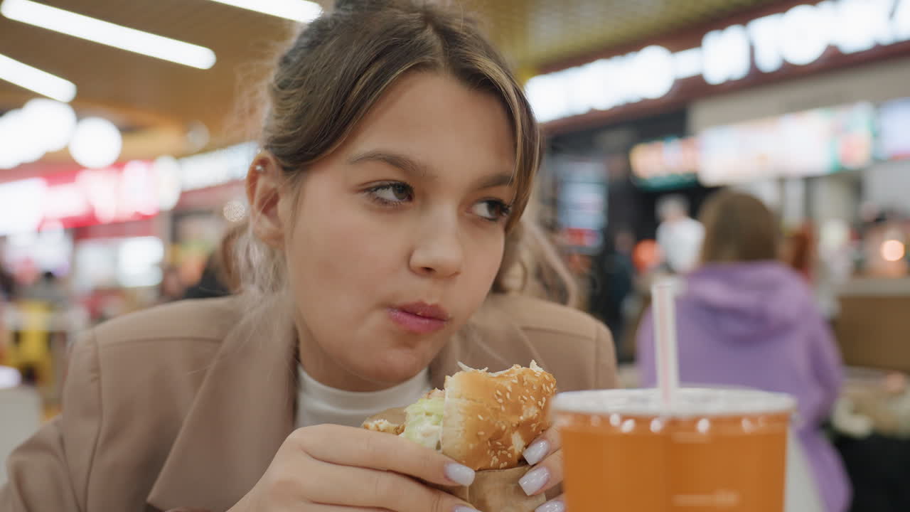 활동적인 사람이 정오에 패스트푸드를 즐기는 모습, 푸드 코트에서 바쁘게 식사하는 사람들의 활기찬 장면, 붐비는 점심시간 환경 속에서 햄버거를 열정적으로 먹는 활기찬 백인 개인