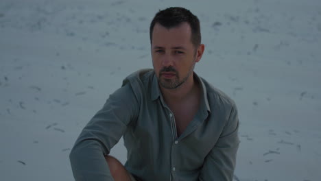 pensive man sitting on a sandy beach at sunset