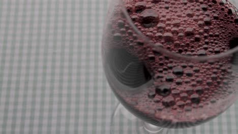 pouring red wine into glass, close-up on gingham cloth background, focus on flow and texture