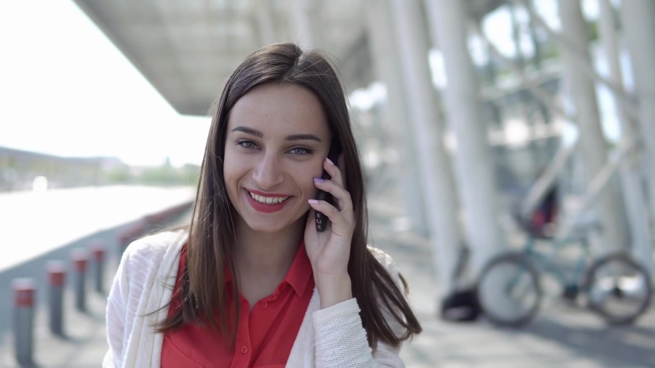 Giovane donna felice che parla allo smartphone e sorride all'aperto