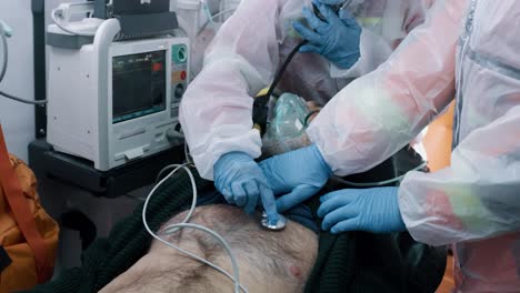 paramedics Listening to Lungs of Patient Tilt down View of Emergency Medicine Workers in Hazmat Suits Using Stethoscope to Listen Lungs of Aged Man with Pneumonia in Ambulance