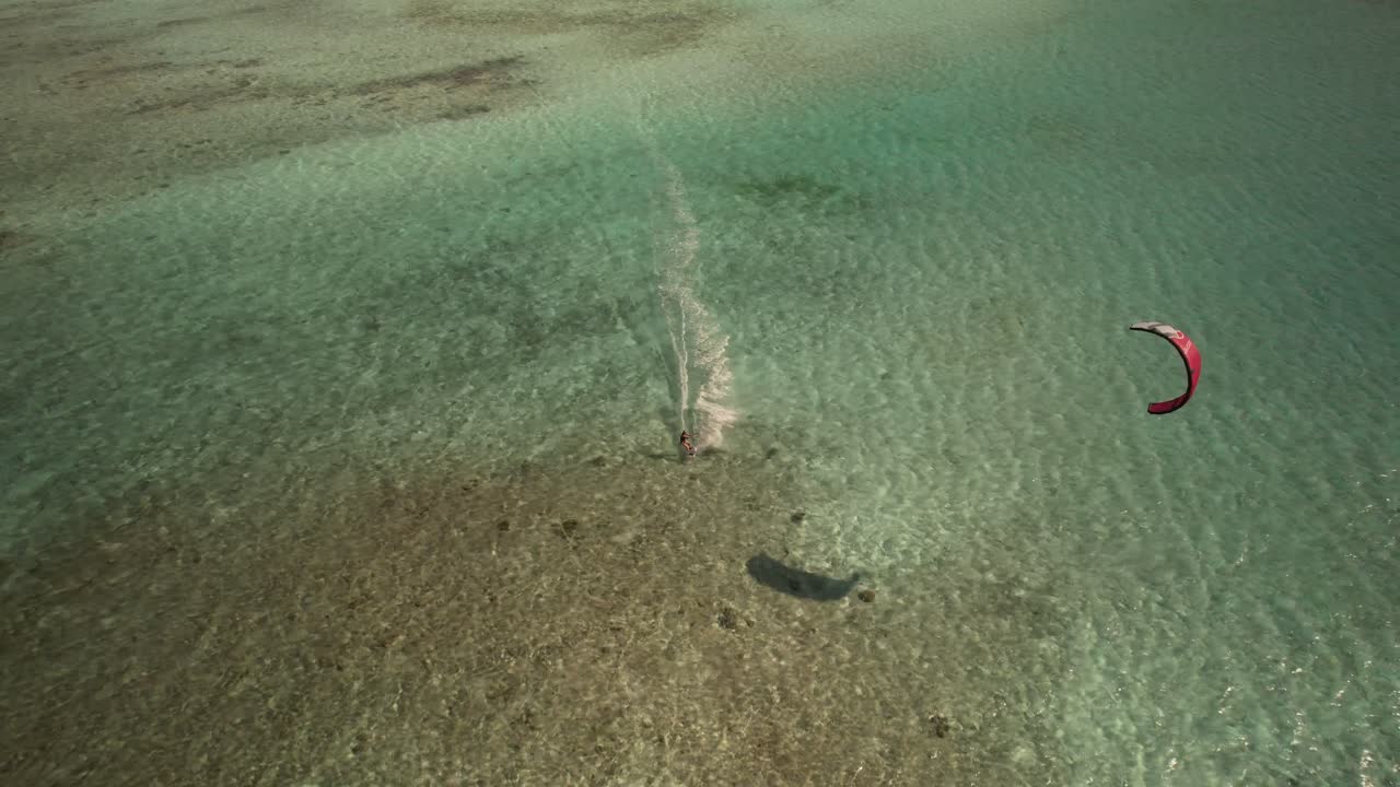 kiteboarder deslizándose en aguas turquesas con una cometa roja vibrante vista desde arriba