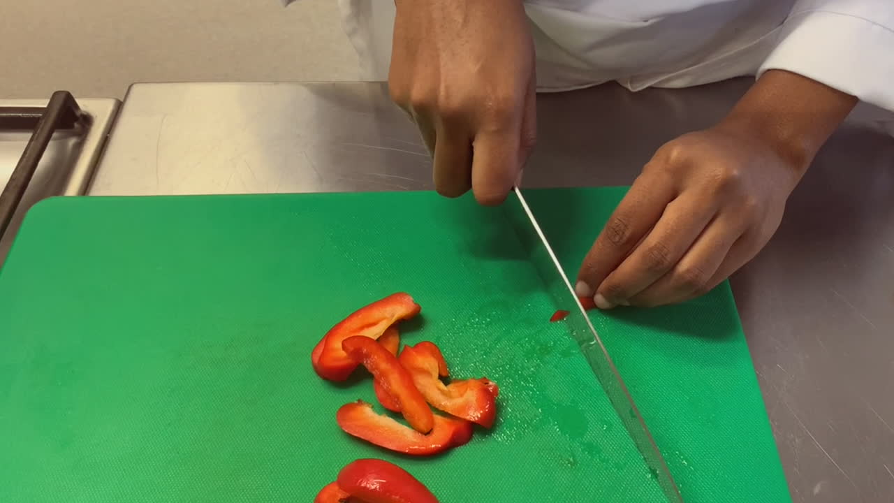 Sweet red bell pepper is diced on green cutting board by young chef