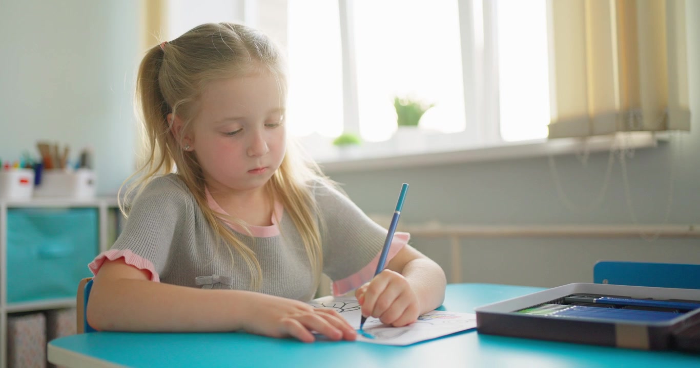 Jong blond meisje kleurt een tekening aan haar bureau