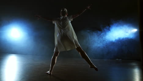 a dramatic scene of modern ballet a lone ballerina in a white dress performs dance steps using modern choreography.