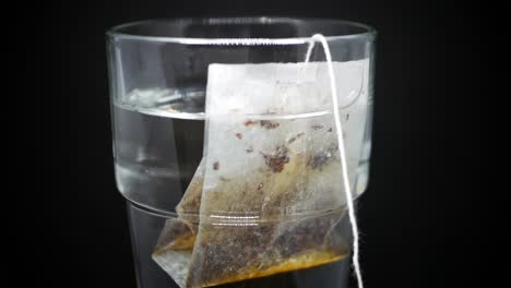 tea bag slowly drift in a clear glass with boiling water and brews it against black background