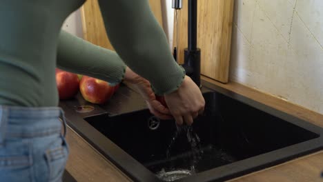 una mujer lava una manzana en el fregadero negro