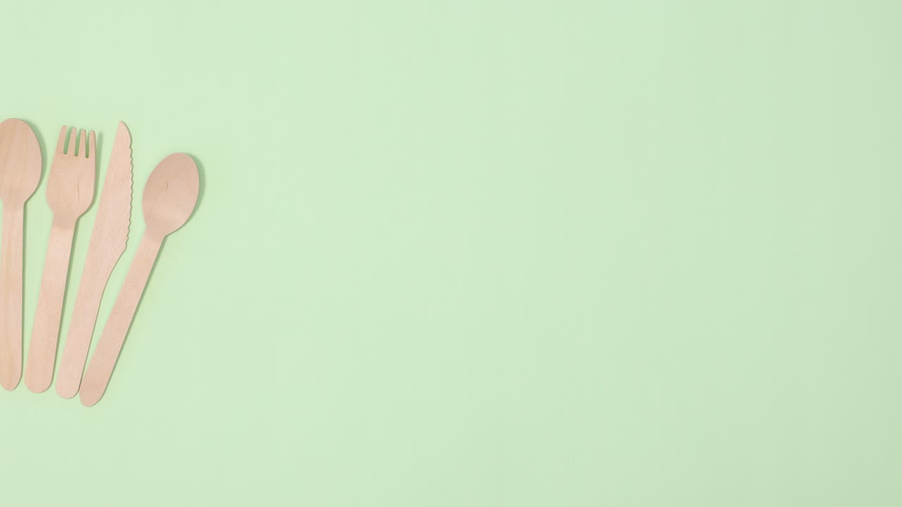 pila de utensilios de cocina ecológicos de cero residuos ordenando en un fondo verde claro.