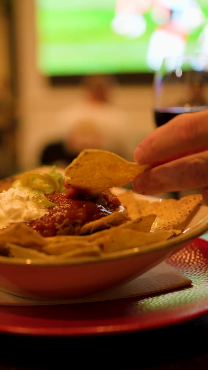Tortilla chips con salsa e panna acida in un'illuminazione calda da bar sportivo, con messa a fuoco ridotta.