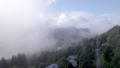 Rising-above-cabin-aerial-with-mountain-slope-and-green-meadows-and-pine-tree-divide-with-cloud-obscuring-half-of-the-valley