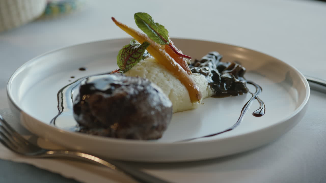 Close-up of a waiter serving a gourmet dish with mashed potatoes, baby carrots, sprouts, and a piece of meat with dark gravy
