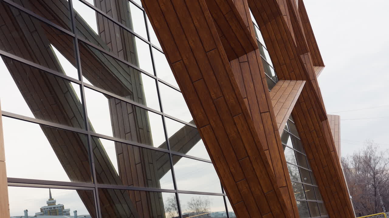 Down to top view of tall fitness building with wood panels and reflective glass windows showing parked cars, houses, and trees outside in urban area under cloudy sky