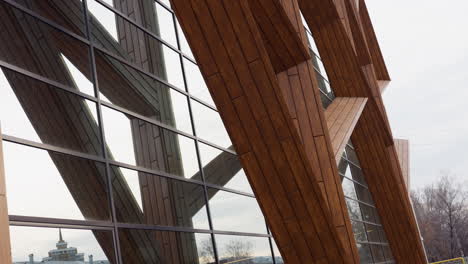 down to top view of tall fitness building with wood panels and reflective glass windows showing parked cars, houses, and trees outside in urban area under cloudy sky
