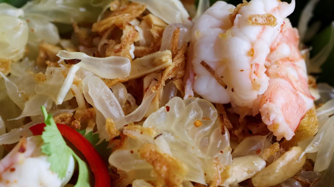 Detailed view of shrimp, pomelo, and crispy shallots with vibrant herbs and chili slices.