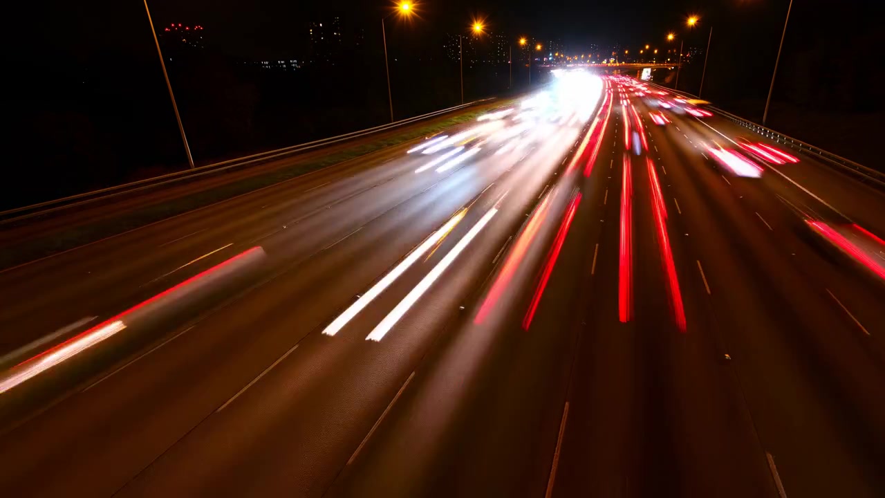 Luci del traffico autostradale notturno che sfrecciano su un cavalcavia, fanali posteriori rossi e fari bianchi che si sfocano in una lunga esposizione.