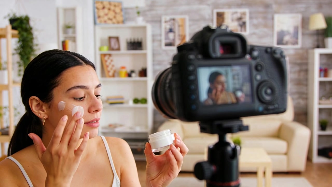 Applying woman in white tank top demonstrating cream on cheeks at home, DSLR recording starting
