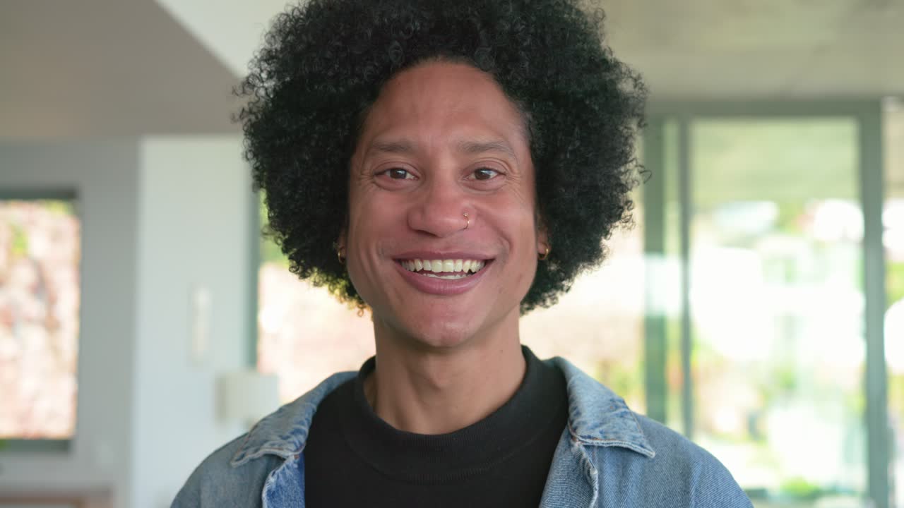 With camera rolling, African American man standing in living area smiling then laughing near plant