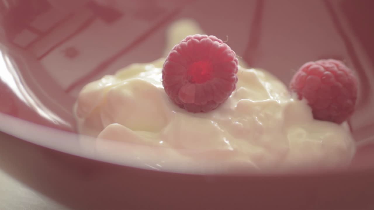 Dropping raspberries into a bowl of yoghurt