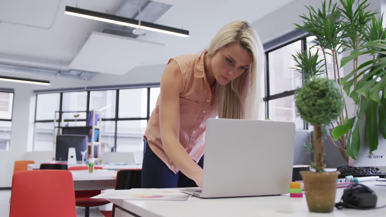 Donna d'affari caucasica che utilizza un laptop ed esamina documenti in un ufficio moderno.